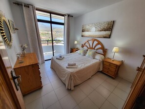 Quarto com cama, mesas de cabeceira, cômoda e vista para o exterior.