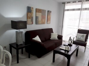 Uma sala de estar com um sofá marrom escuro, uma poltrona combinando, uma mesa de centro, um abajur e três quadros abstratos na parede.