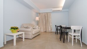 Un espace de vie compact comprenant un canapé, une petite table avec un panier de fleurs, une table à manger avec des chaises et un rideau.