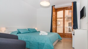 Une chambre à coucher comprenant un lit, un bureau, une télévision et un balcon avec une porte en bois.