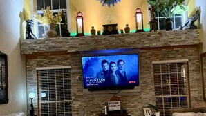 A living room with a stone fireplace, a mounted TV displaying 'The Haunting of Bly Manor', and a 'Welcome Home' sign. - 2,300 Sqft 2 Story Home With 3 Bedrooms 21/2 Bathrooms in Apex North Carolina (Apex)