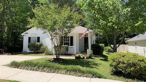 A single-story house with a front porch, a small tree, and an American flag.