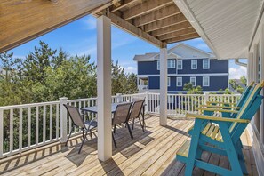 A covered outdoor deck with a table and chairs, a white railing, and a view of a two-story building in the background.