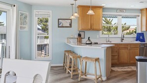 Una cocina con armarios de madera, una isla con taburetes e iluminación colgante, y vistas al exterior por la ventana.