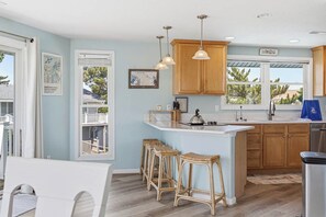A kitchen with wooden cabinets, a bar island with stools, pendant lighting, and a view through the window.