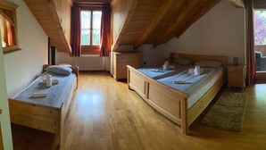 Une chambre avec un plafond en pente, un plancher en bois, un lit avec des oreillers et des serviettes, une commode et une fenêtre avec des rideaux.