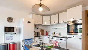 A modern kitchen with white cabinets, a microwave, a refrigerator, an oven, and a dining table set for four. - L'Annexe du Cosmopolitain | Luxury Building | 4 Guests (Honfleur)