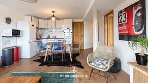 A compact living space with a kitchenette, dining area, and a seating area with a chair and a potted plant. - L'Annexe du Cosmopolitain | Luxury Building | 4 Guests (Honfleur)