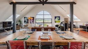 Un espace repas doté d’un plafond haut, d’une grande fenêtre et offrant une vue sur l’extérieur.