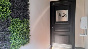 Une porte en bois sombre, sur laquelle on peut lire l’inscription « THE LOFT », et un paillasson sur lequel est écrit : « SAVOURER LES PETITS BONHEURS ».