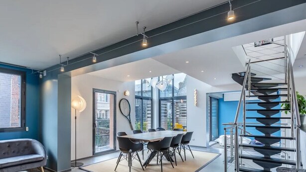 Un interior moderno con comedor, escalera y ventanas amplias.
