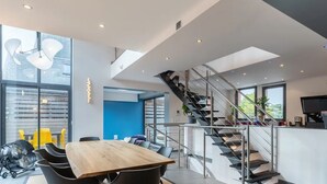 Un interior moderno con una escalera, una zona de comedor y amplios ventanales.