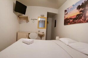 A hotel room with a bed, a TV mounted on the wall, a sink, and a painting of a landscape. - Esquina Batel Hotel (Curitiba)