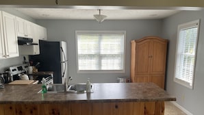 Eine Küche mit Granit Arbeitsplatte, weißen Schränken, einem Holzschrank, einem Kühlschrank, einem Herd und einem Fenster mit Jalousien.