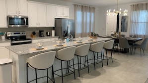 Una cocina moderna con armarios blancos, electrodomésticos de acero inoxidable y una isla central con taburetes de bar.