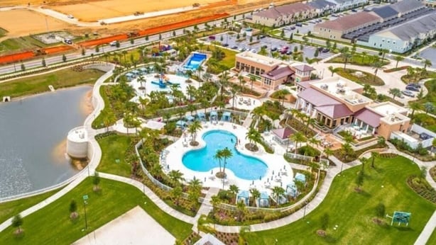 Vista aérea de un resort con una piscina central, un tanque de agua grande y un estacionamiento con varios edificios.