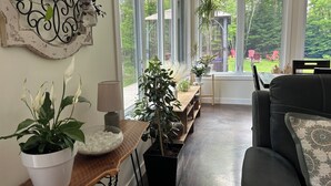 Un salon chaleureux avec une grande fenêtre, un canapé en cuir noir et diverses plantes en pot.