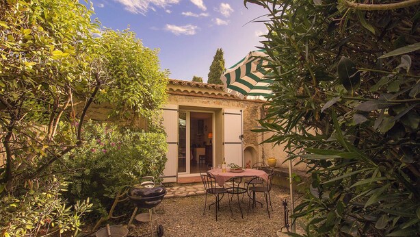 A patio area with a table and chairs, a grill, and a stone pathway. - Maison des Genets (N°6) (Marcorignan)