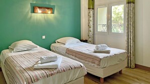 A room with two beds, a window with curtains, and a wall-mounted light fixture. - Maison des Genets (N°6) (Marcorignan)
