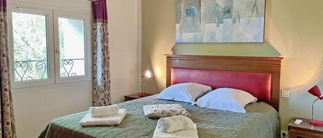 A hotel room with a bed, a painting on the wall, and a window with curtains.