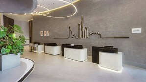 Een modern hotel ontvangstgebied met een minimalistisch ontwerp, met een receptiebalie, een grote potplant en een kunstwerk aan de muur.