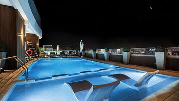 A rooftop swimming pool with a city view at night.