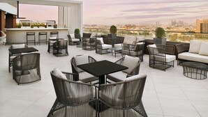 Een terras met rieten meubilair, een bar en uitzicht op de stad.