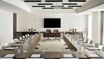 Een vergaderzaal met een lange tafel, stoelen, een groot flatscreen-televisie en een whiteboard.