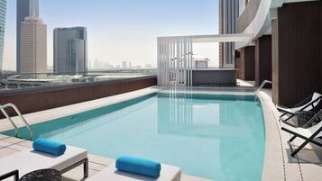Une piscine sur le toit, dotée de chaises longues et offrant une vue sur la ville.