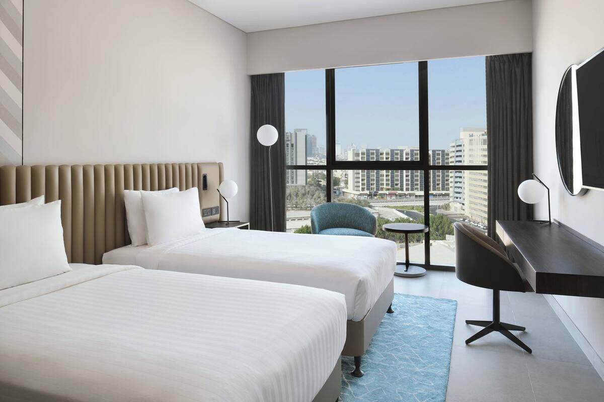 Une chambre d’hôtel avec deux lits, un bureau, une chaise et une grande fenêtre donnant sur la ville.