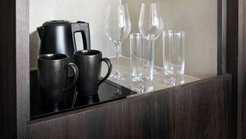 Espejo de madera oscura que refleja una cafetera, dos tazas negras y tres copas de vino transparentes sobre una encimera.