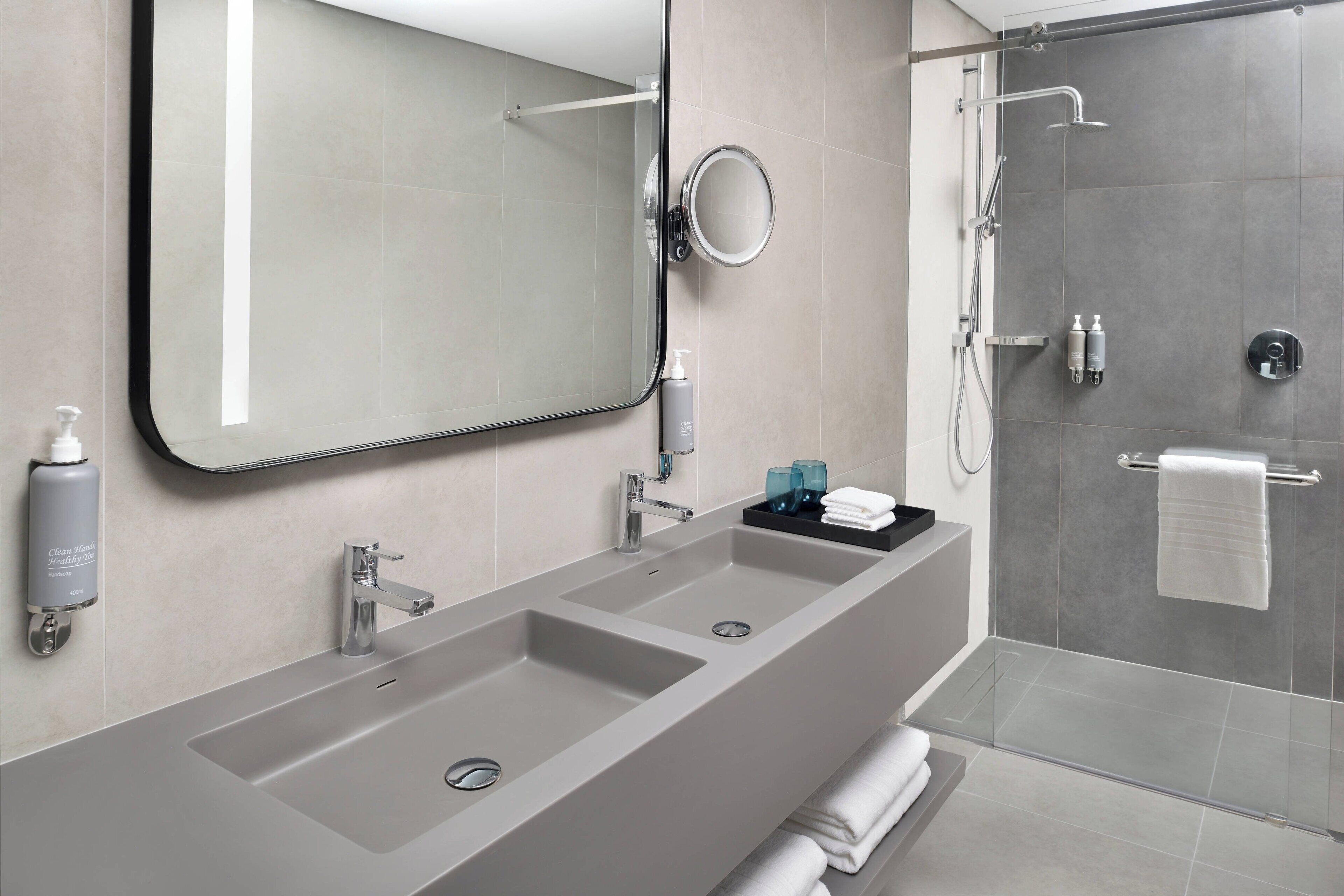 Une salle de bain moderne avec un grand miroir, deux lavabos, une douche et un porte-serviettes.