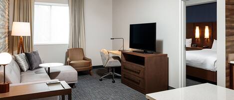Habitación de hotel con sofá, escritorio, televisor, cama y mesita de noche.