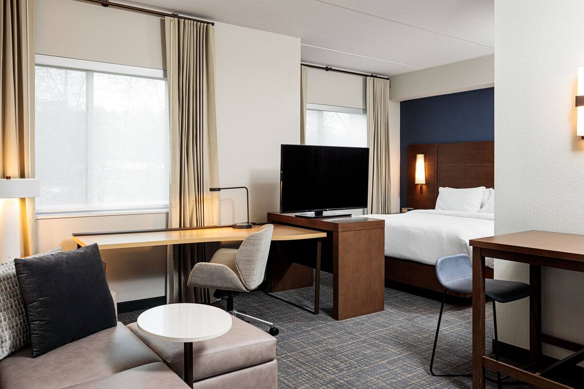A hotel room with a bed, desk, television, and seating area.