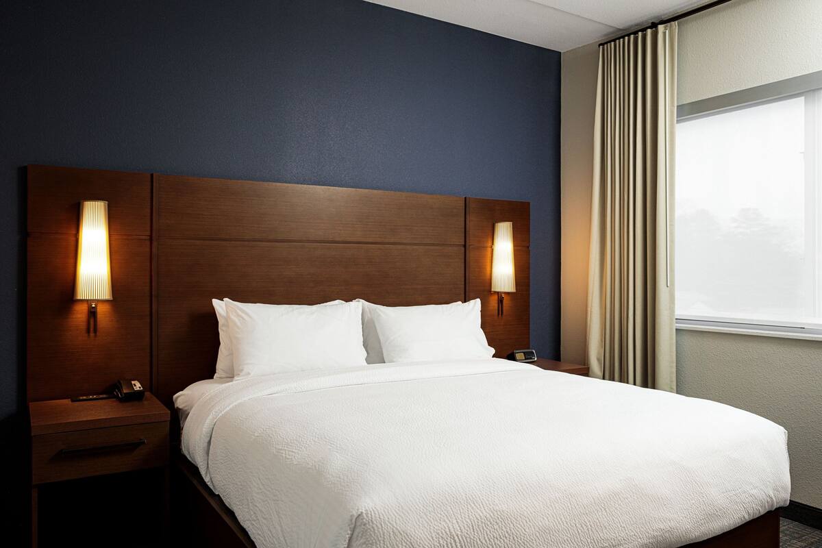 A hotel room with a large bed, two bedside lamps, a nightstand, and a window with curtains.