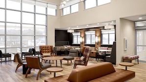 Un vestíbulo amplio con techos altos, ventanas grandes y diversas opciones de asiento, incluyendo sofás, sillones y mesas.