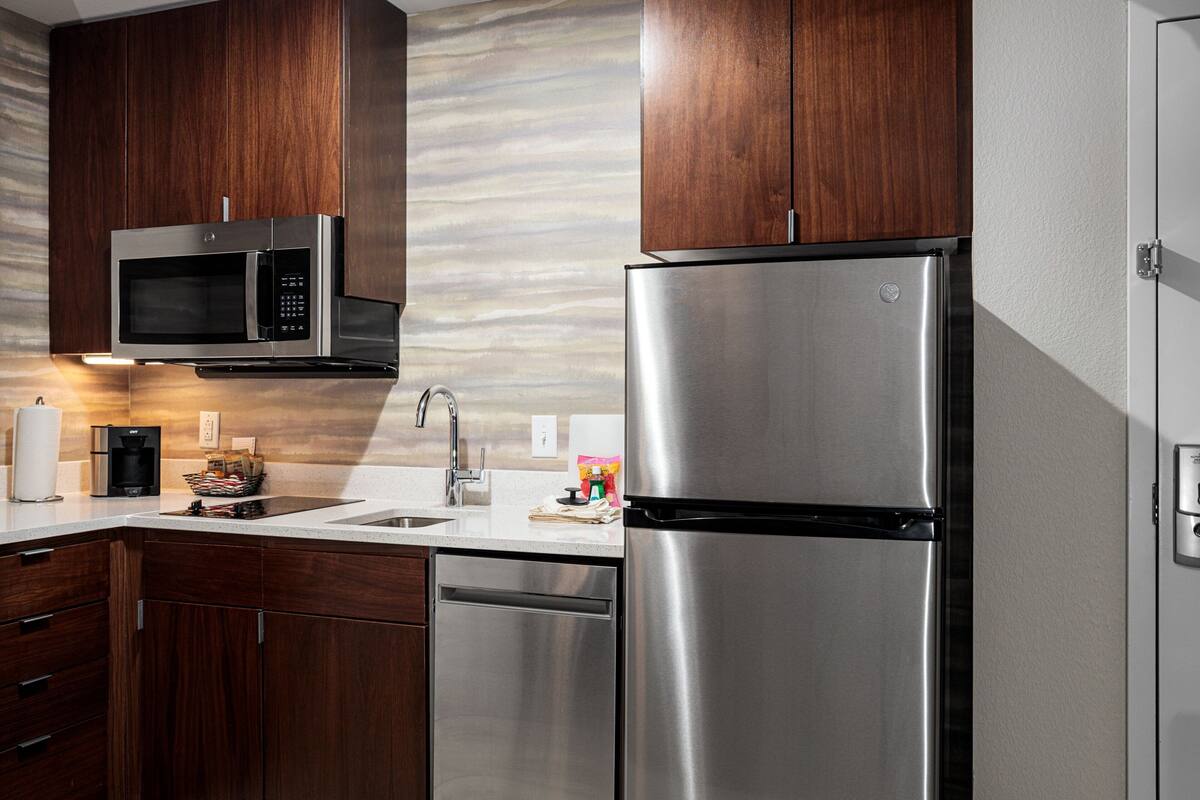 A modern kitchen with stainless steel appliances, wooden cabinets, and a white countertop.