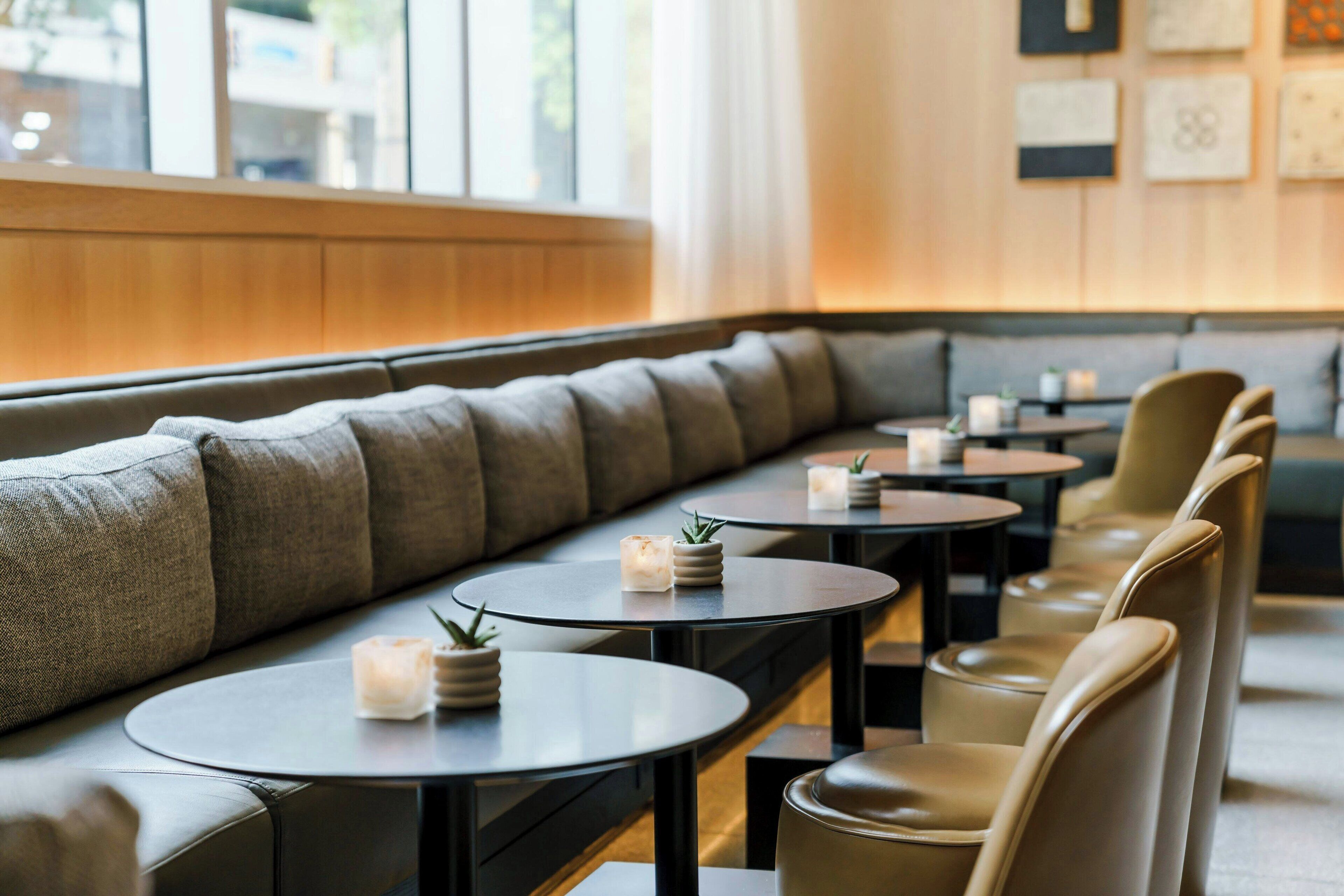 Un restaurante moderno con una larga zona de asientos tipo banco, mesas redondas y centros de mesa con velas.