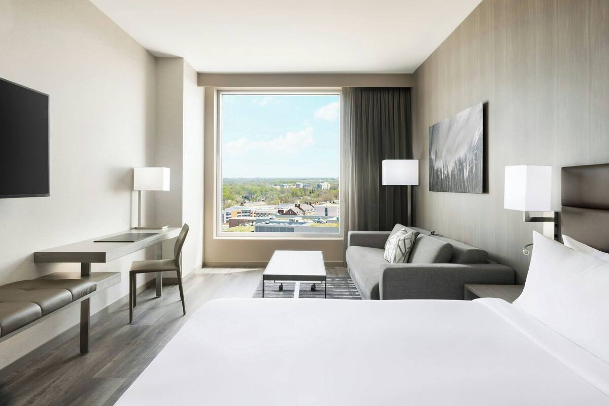 Een hotelkamer met een groot raam, een bed, een bank, een bureau en een stoel.