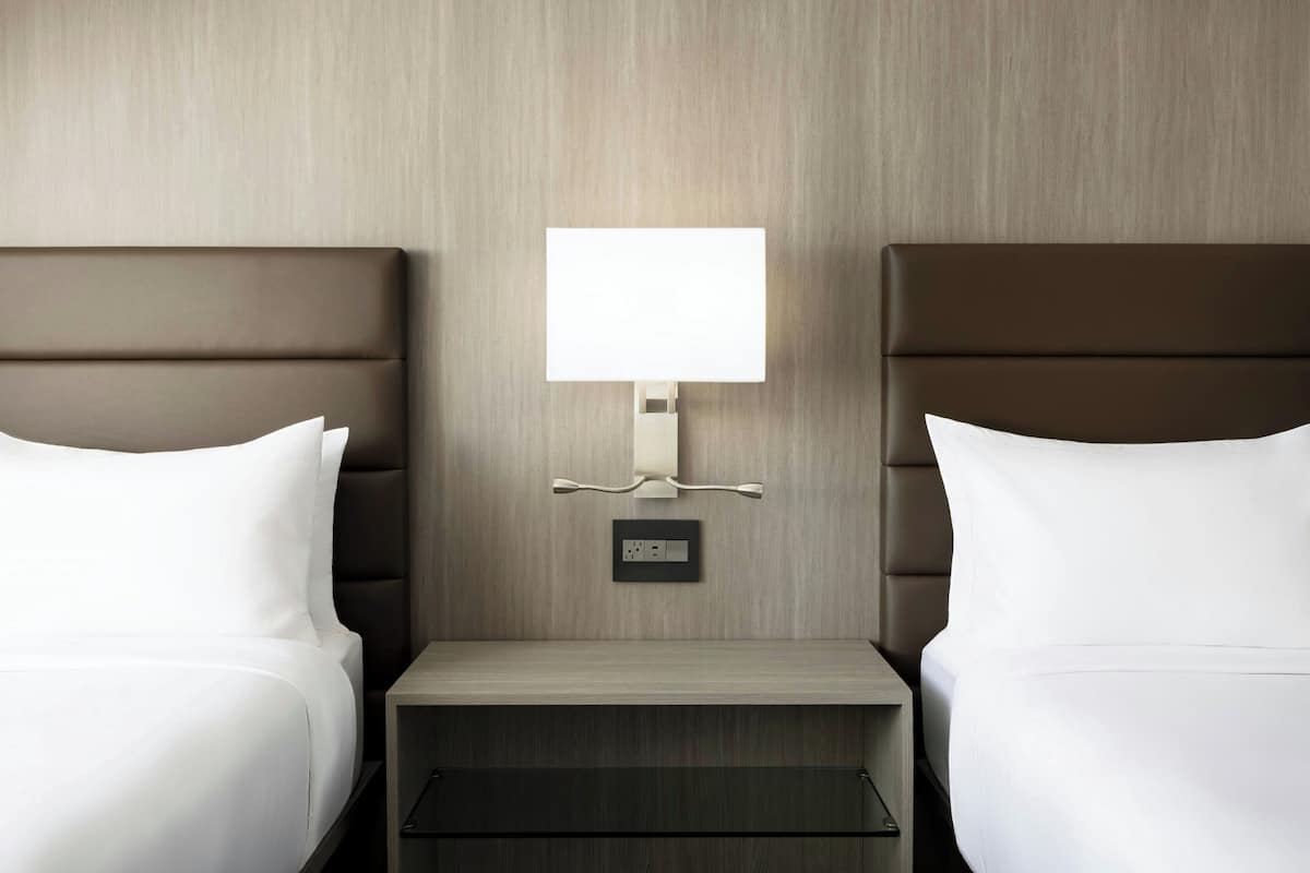 Een hotelkamer met twee bedden, een nachtkastje, een lamp en een stopcontact.
