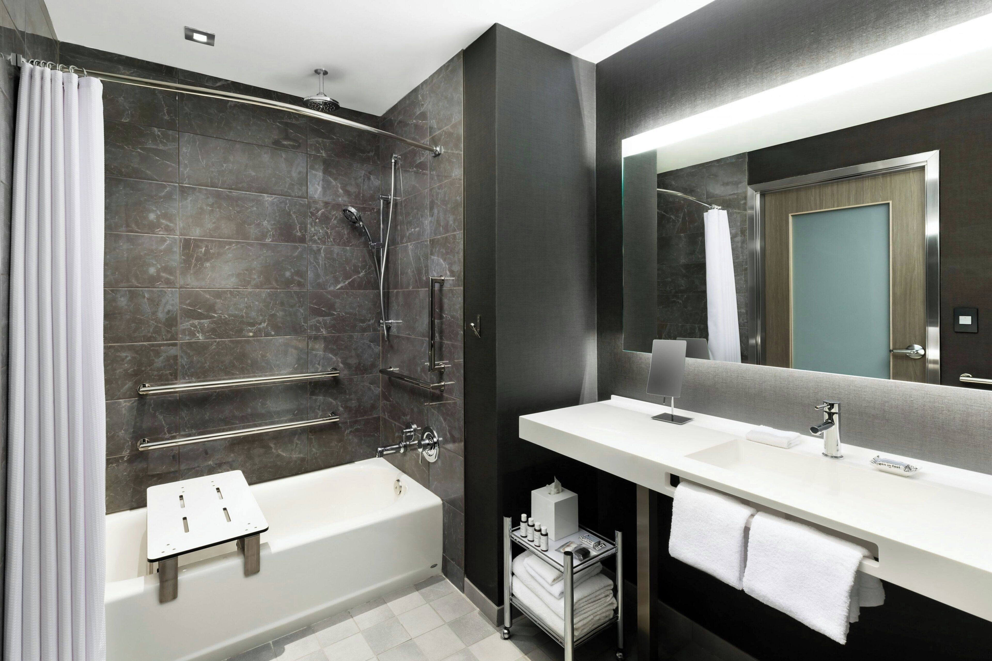 A modern bathroom with a bathtub, shower, vanity, and a large mirror.