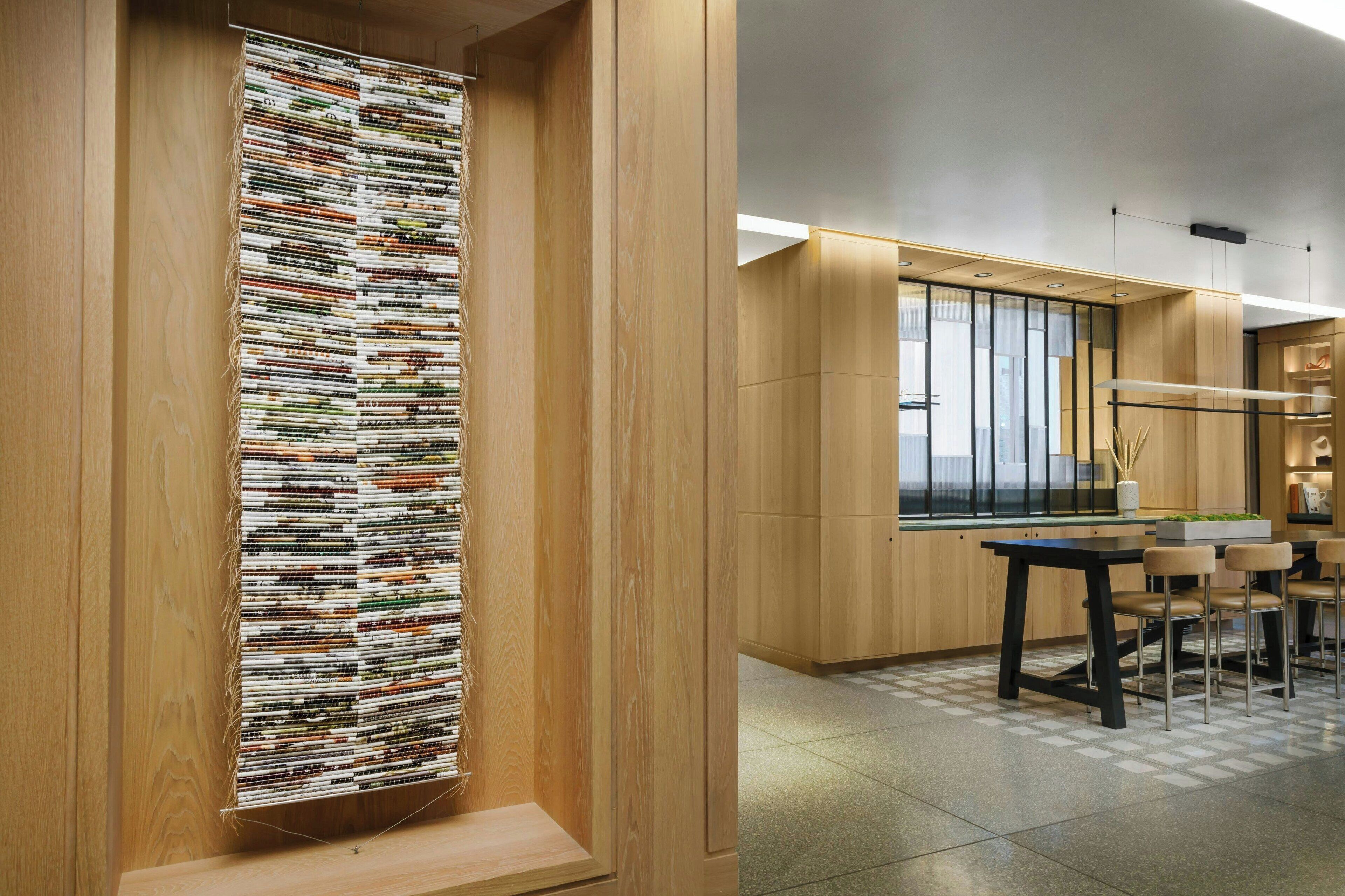 A modern interior with a wooden wall, a long vertical textile artwork, and a dining area with a table and chairs.