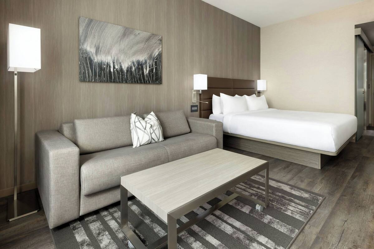 Hotelkamer met een bank, een bed, een bijzettafeltje, een schilderij en twee wandlampen.