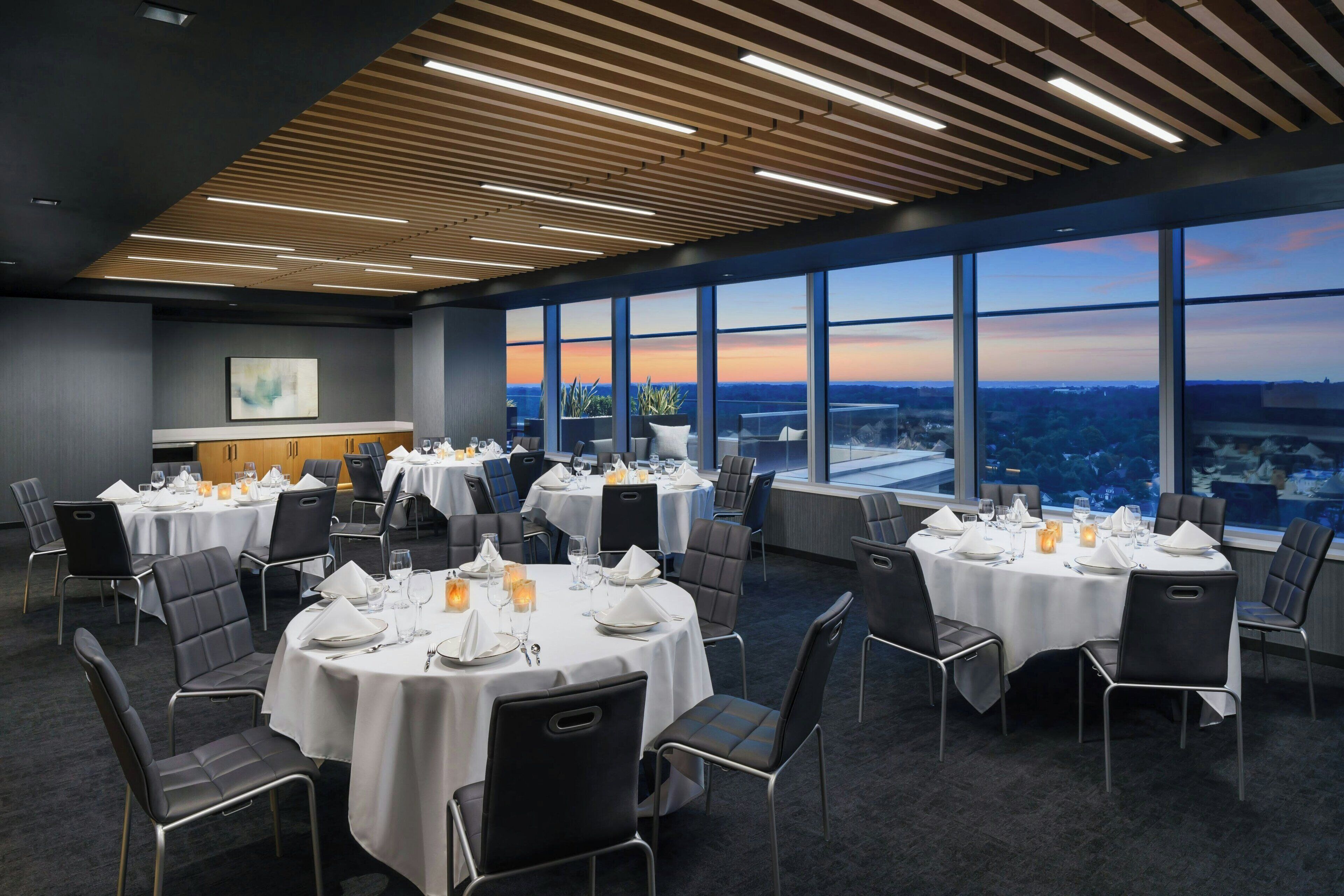 A conference room with round tables, black chairs, and a city view through large windows.