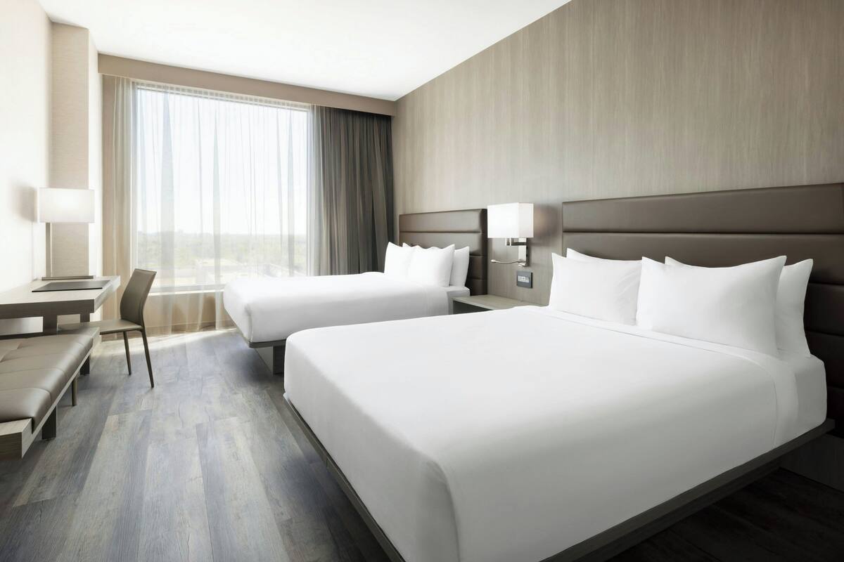 Een hotelkamer met twee bedden, een bureau, een stoel en een groot raam.