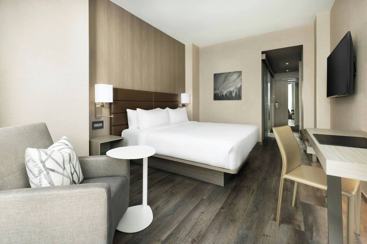 Een moderne hotelkamer met een groot bed, een bank, een klein rond tafeltje en een aan de muur bevestigde televisie.
