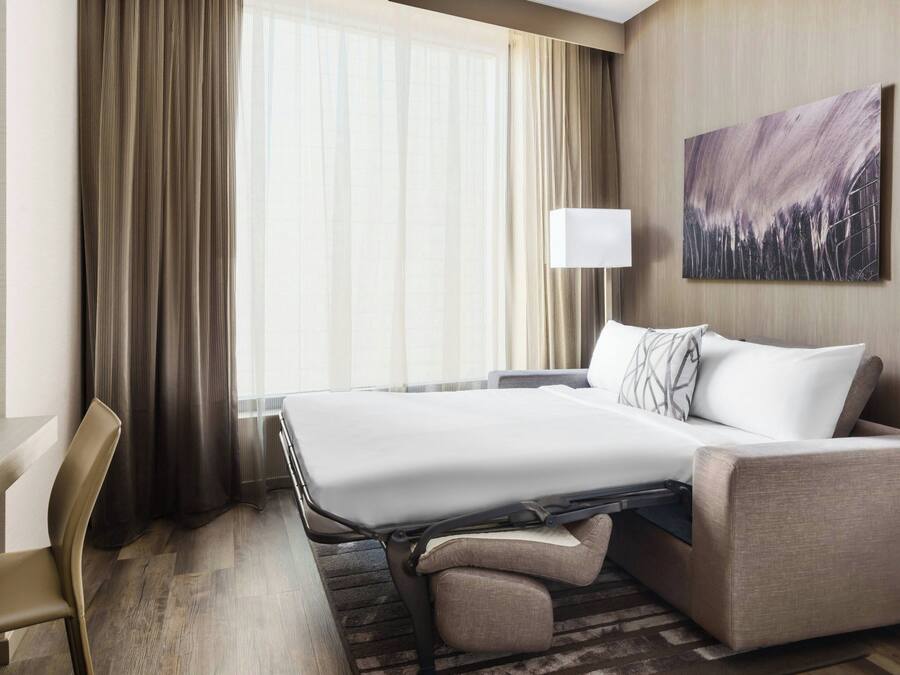 A hotel room with a bed, a desk, a chair, a sofa, a lamp, and a painting on the wall.