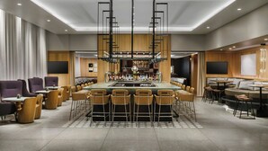 A modern bar area with a central island, bar stools, and a seating area with couches and tables. - AC Hotel by Marriott Bethesda Downtown (Bethesda)
