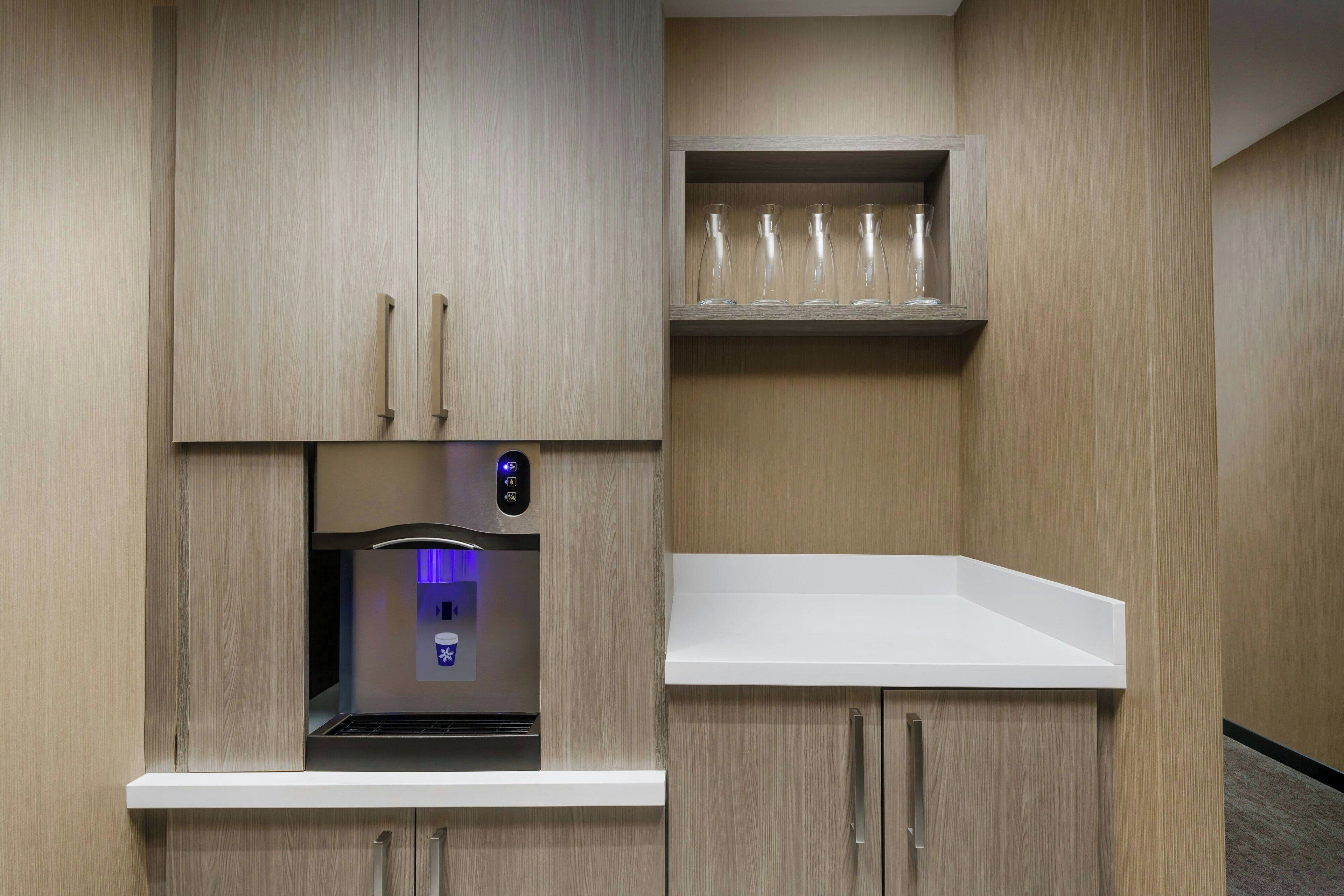 A kitchenette with a built-in coffee machine, a shelf with glasses, and a white countertop.