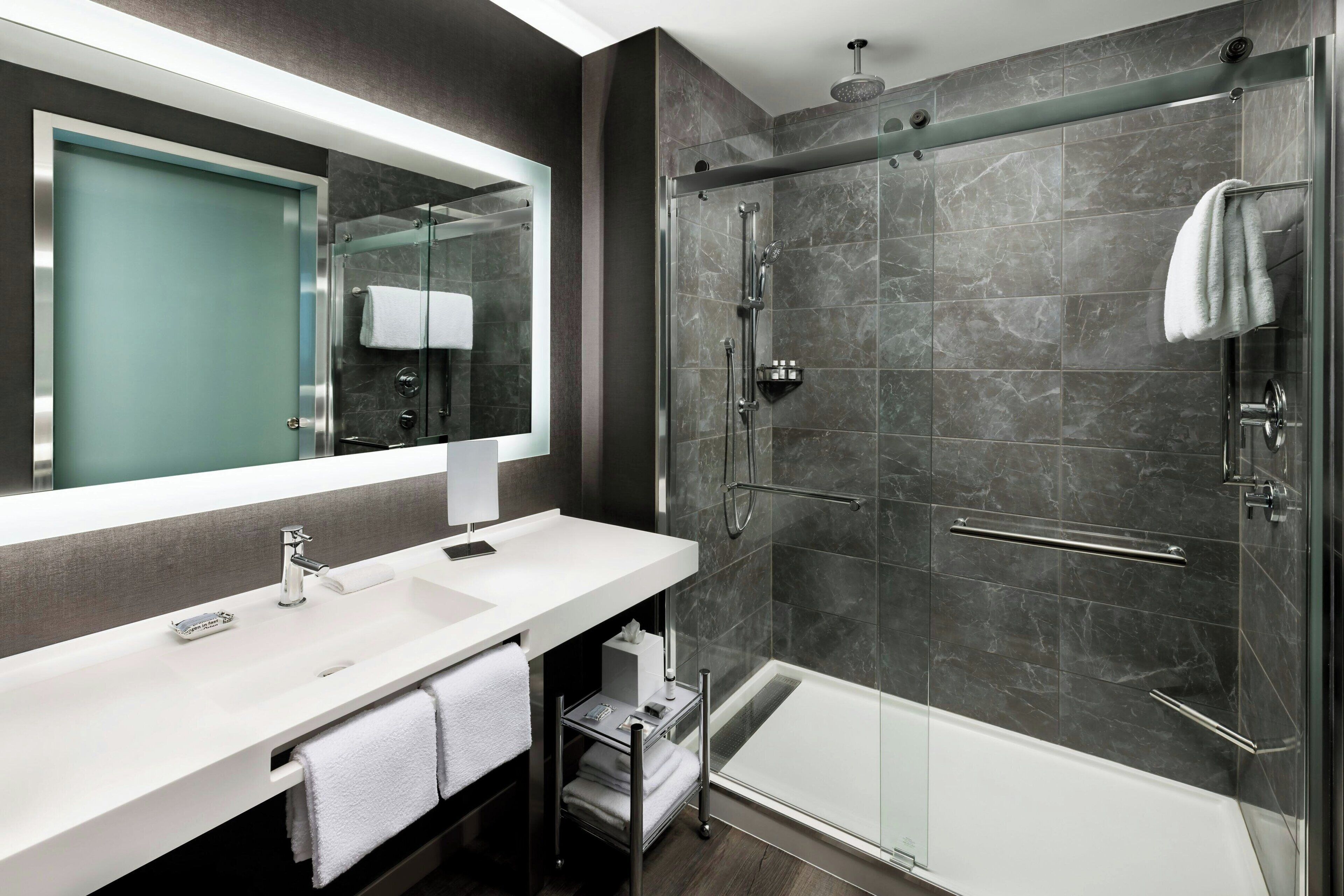 A modern bathroom with a large mirror, two sinks, a shower, and a glass-enclosed shower area.